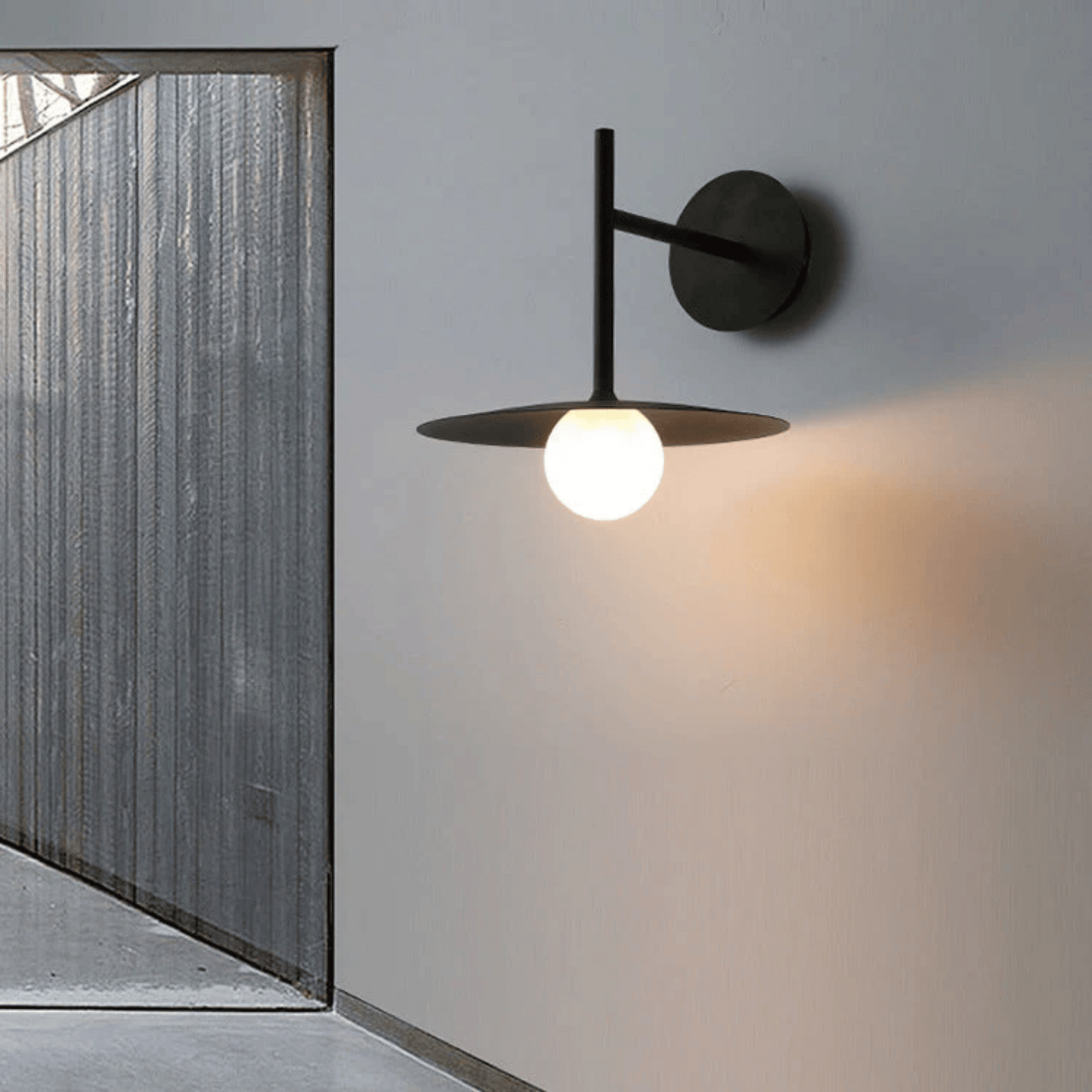 Modern wall-mounted light fixture on a gray wall with a glass door in the background.