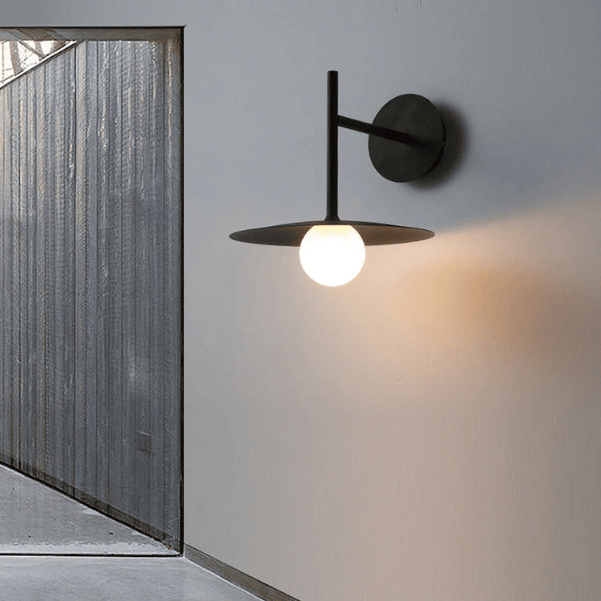 Modern wall-mounted light fixture on a gray wall with a glass door in the background.
