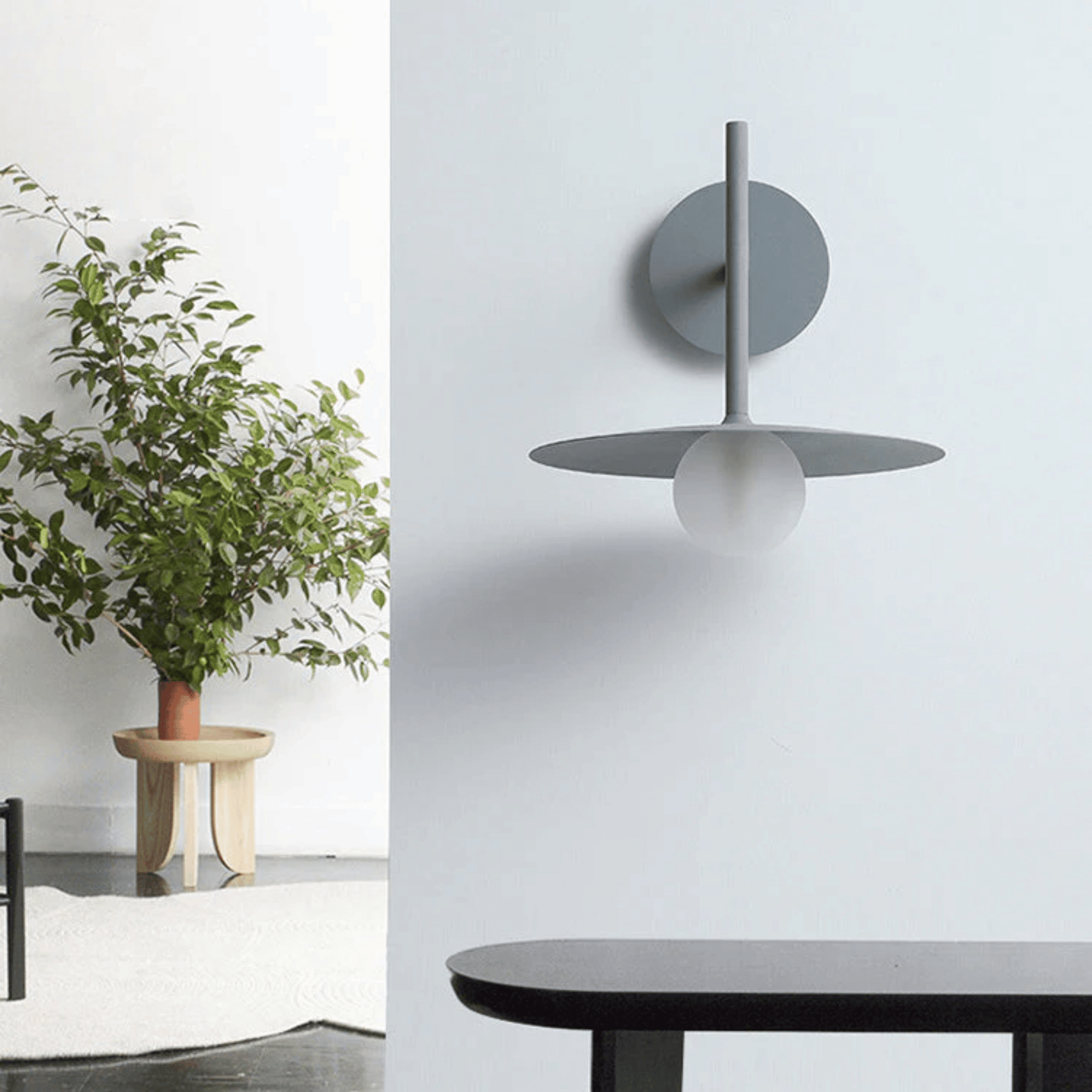 Modern wall sconce with a plant and table in a minimalistic room.