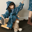 Child in a blue robe with white patterns sitting on a wooden horse toy with a teddy bear.