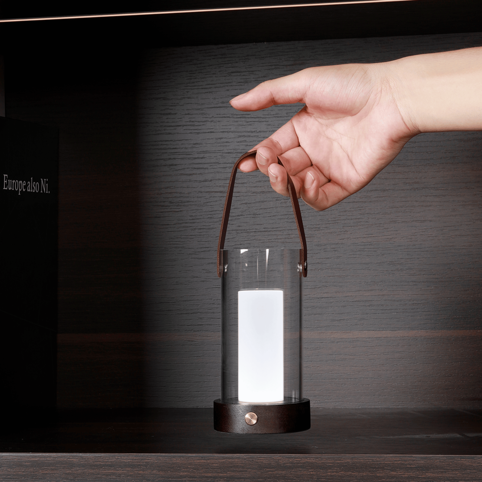 Hand holding a glass lantern with a light inside against a dark background