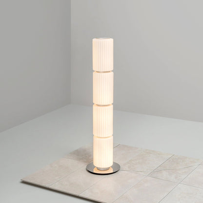 Slim ribbed-glass floor lamp glowing warmly against a light gray wall.