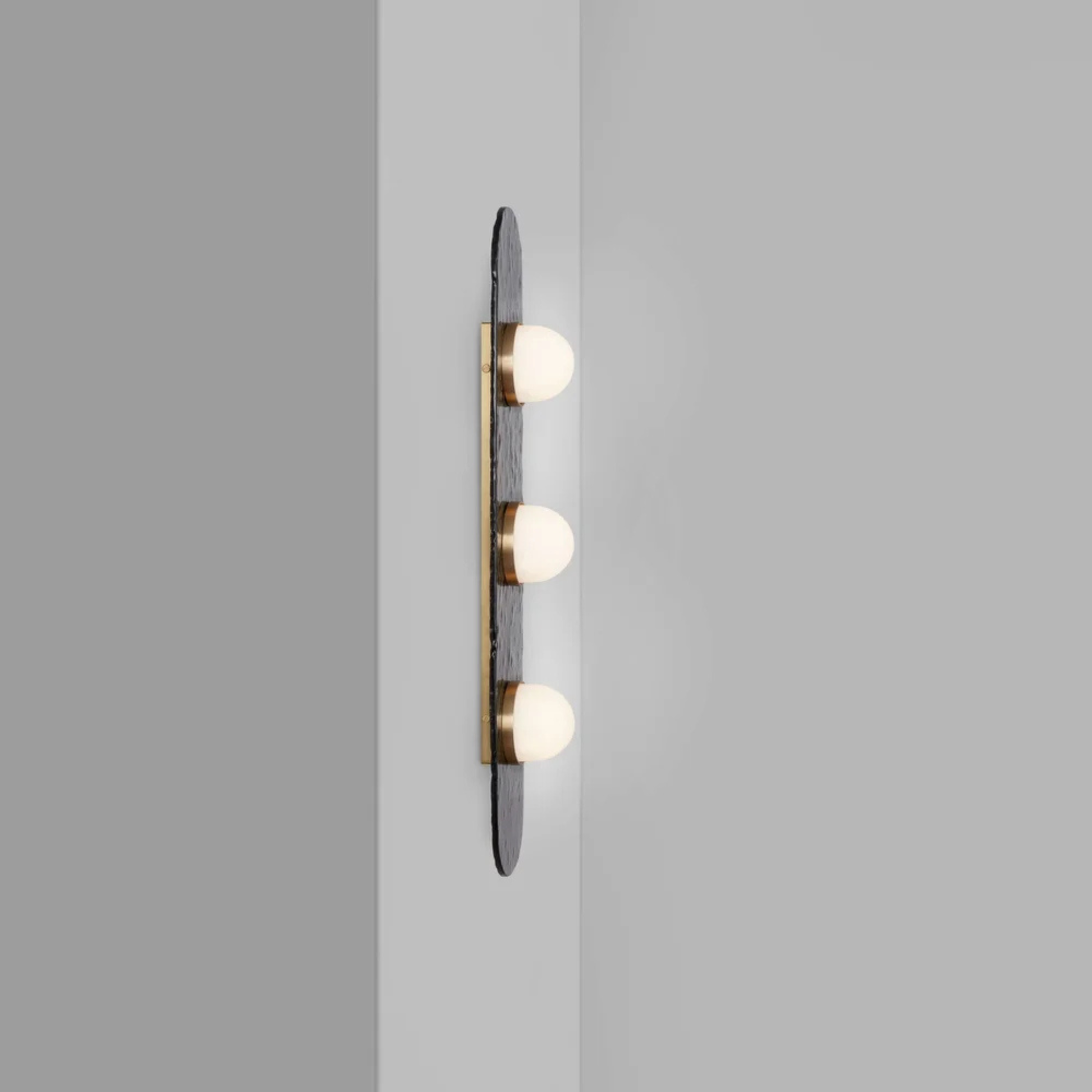 three bulb sconce viewed from the side mounted on a light grey wall