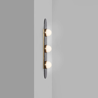 three bulb sconce viewed from the side mounted on a light grey wall