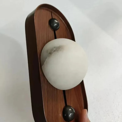 Handheld view of the wooden wall lamp with matte marble globe and black knobs.