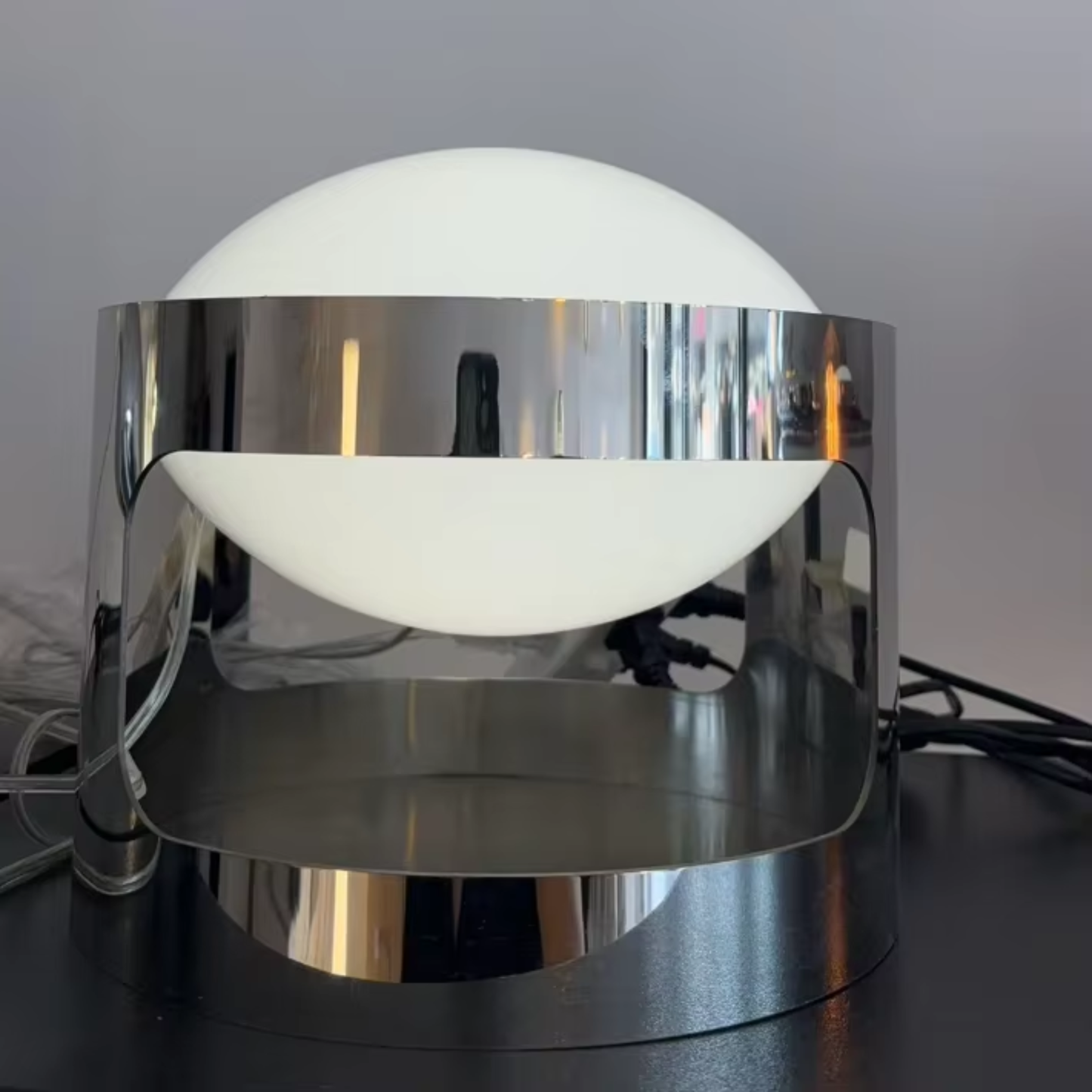 Modern table lamp with chrome base and white globe shade on a dark surface.