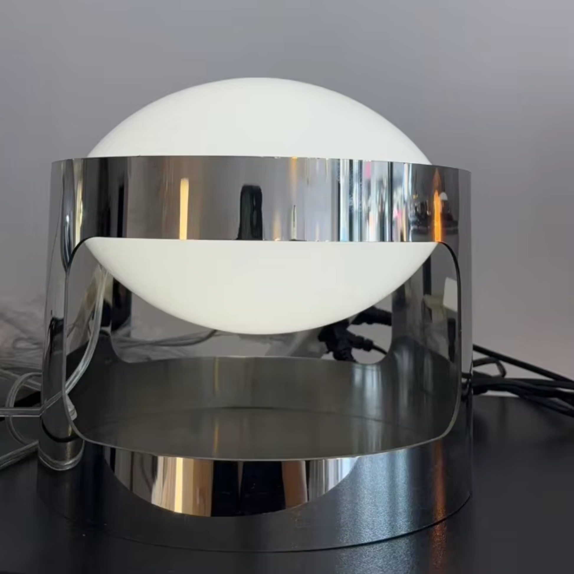 Modern table lamp with chrome base and white globe shade on a dark surface.