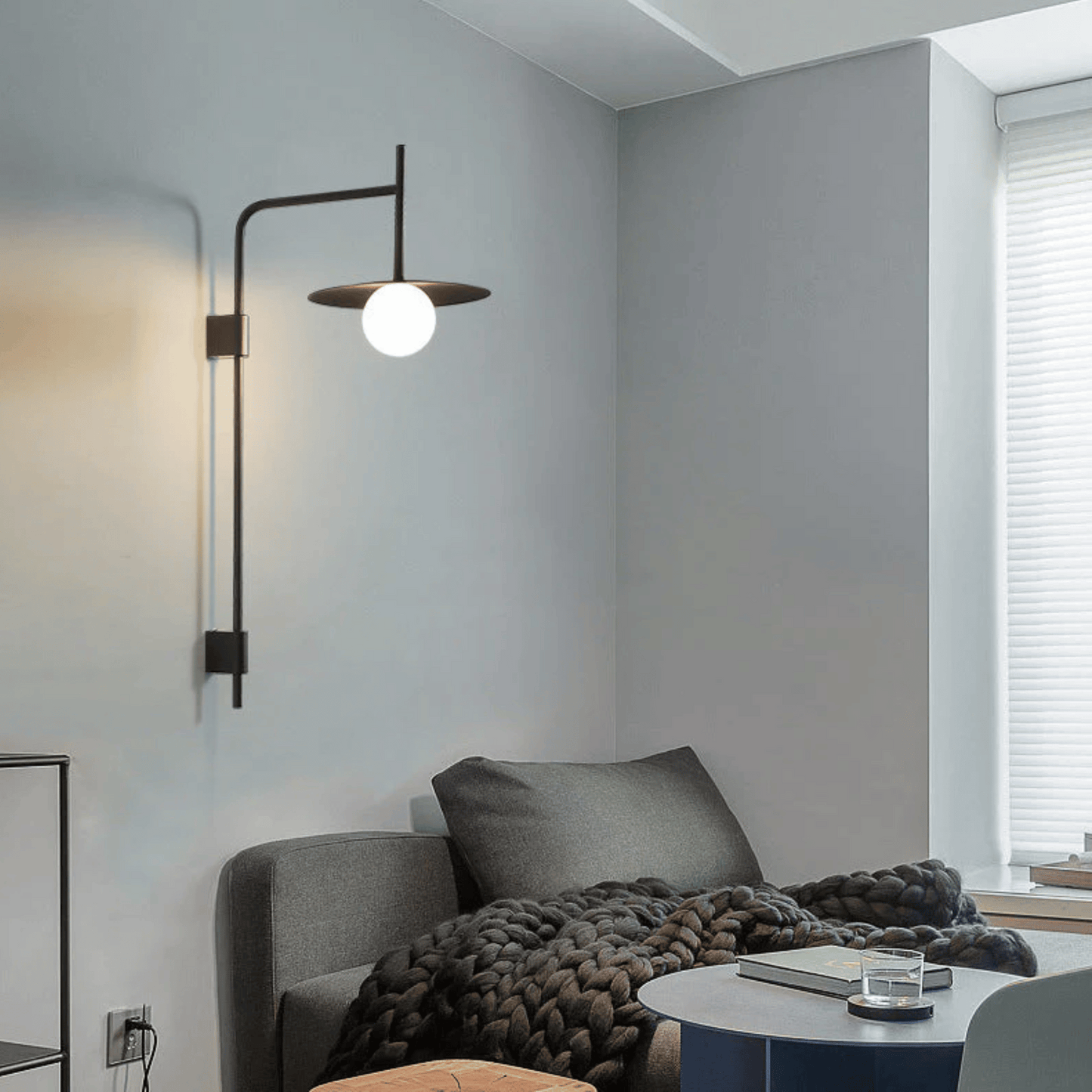 Modern living room with a gray sofa, throw blanket, and wall-mounted lamp.