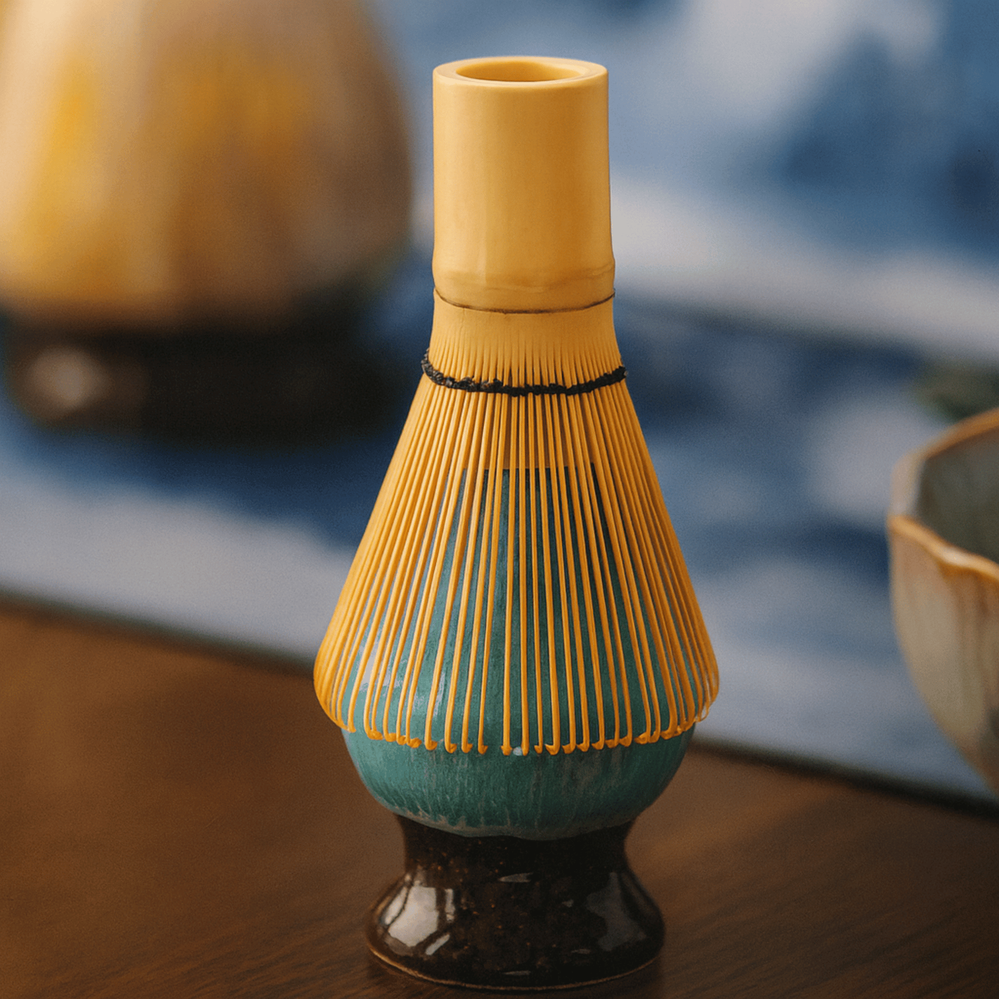 Ceramic whisk holder with yellow top and blue base on a wooden surface