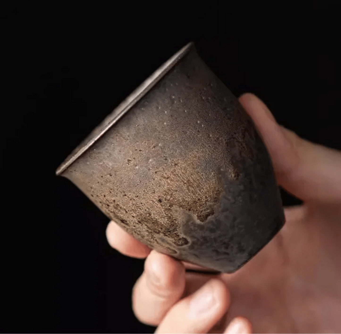Hand holding a textured ceramic cup against a dark background
