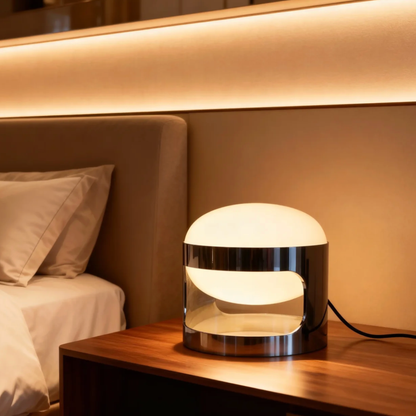 Modern bedside lamp on a wooden nightstand next to a bed with beige pillows.