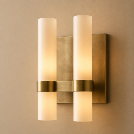 Wall-mounted light fixture with brass finish and cylindrical glass shades on a beige wall.