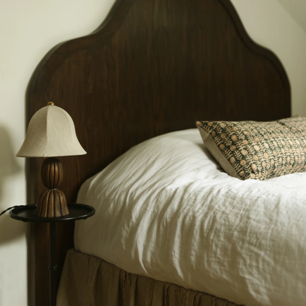 Bed with wooden headboard and lamp, featuring a textured pillow.