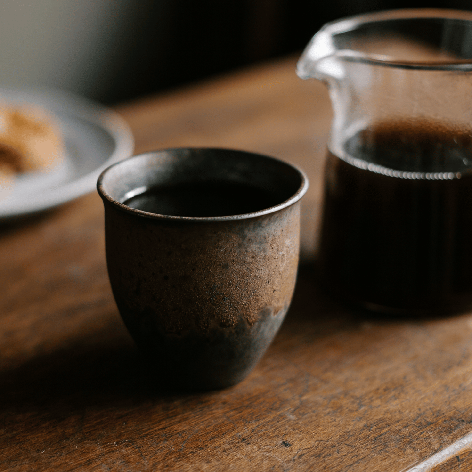 Black ceramic cup and glass teapot on a wooden table with a blurred background