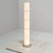 Vertical multi-segment ribbed-glass floor lamp illuminated on a smooth white floor.