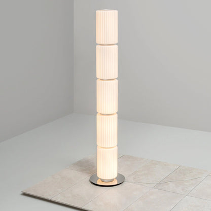 Vertical multi-segment ribbed-glass floor lamp illuminated on a smooth white floor.