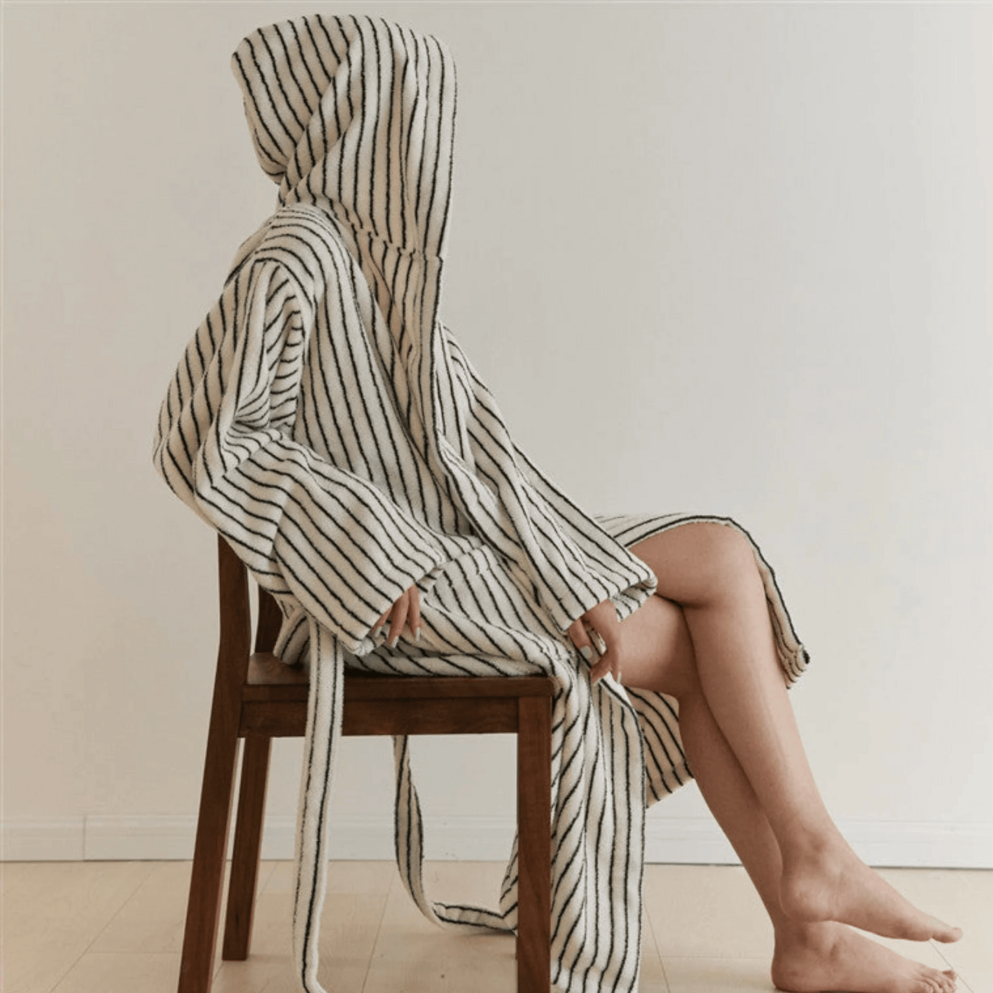 Person wrapped in a striped towel sitting on a wooden chair against a plain background