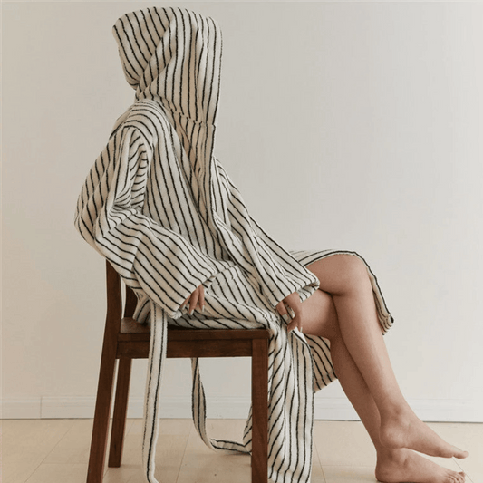 Person wrapped in a striped towel sitting on a wooden chair against a plain background