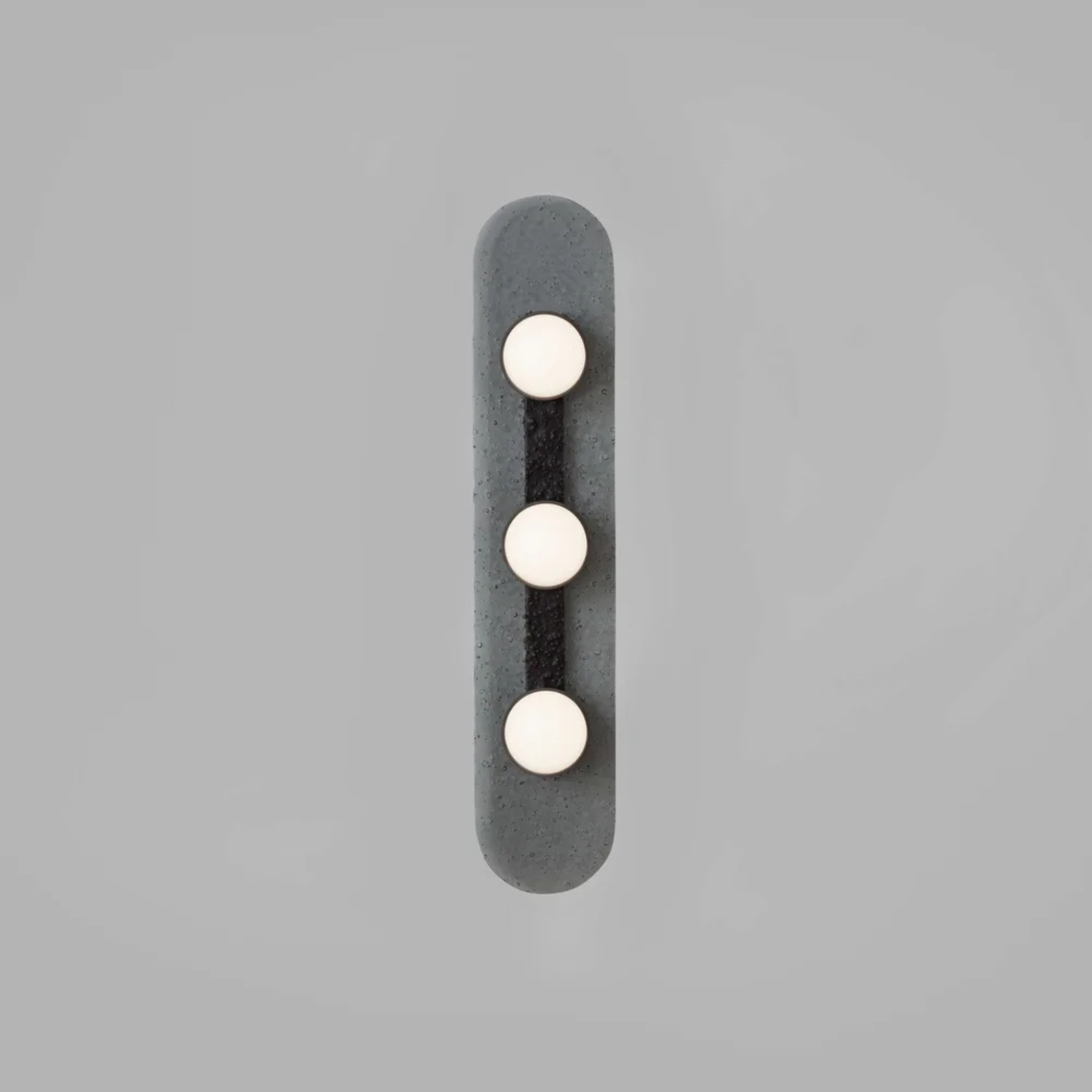 vertical grey wall sconce with three round warm white bulbs arranged in a straight line on a textured elongated backplate