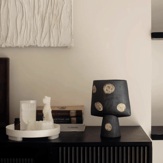 Black lamp with circular patterns on a dark surface, with a neutral wall in the background