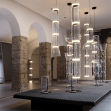 Modern chandelier display in a room with stone arches and concrete floor.