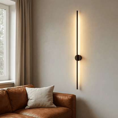 Modern wall sconce on a neutral wall next to a brown leather sofa with a white pillow.