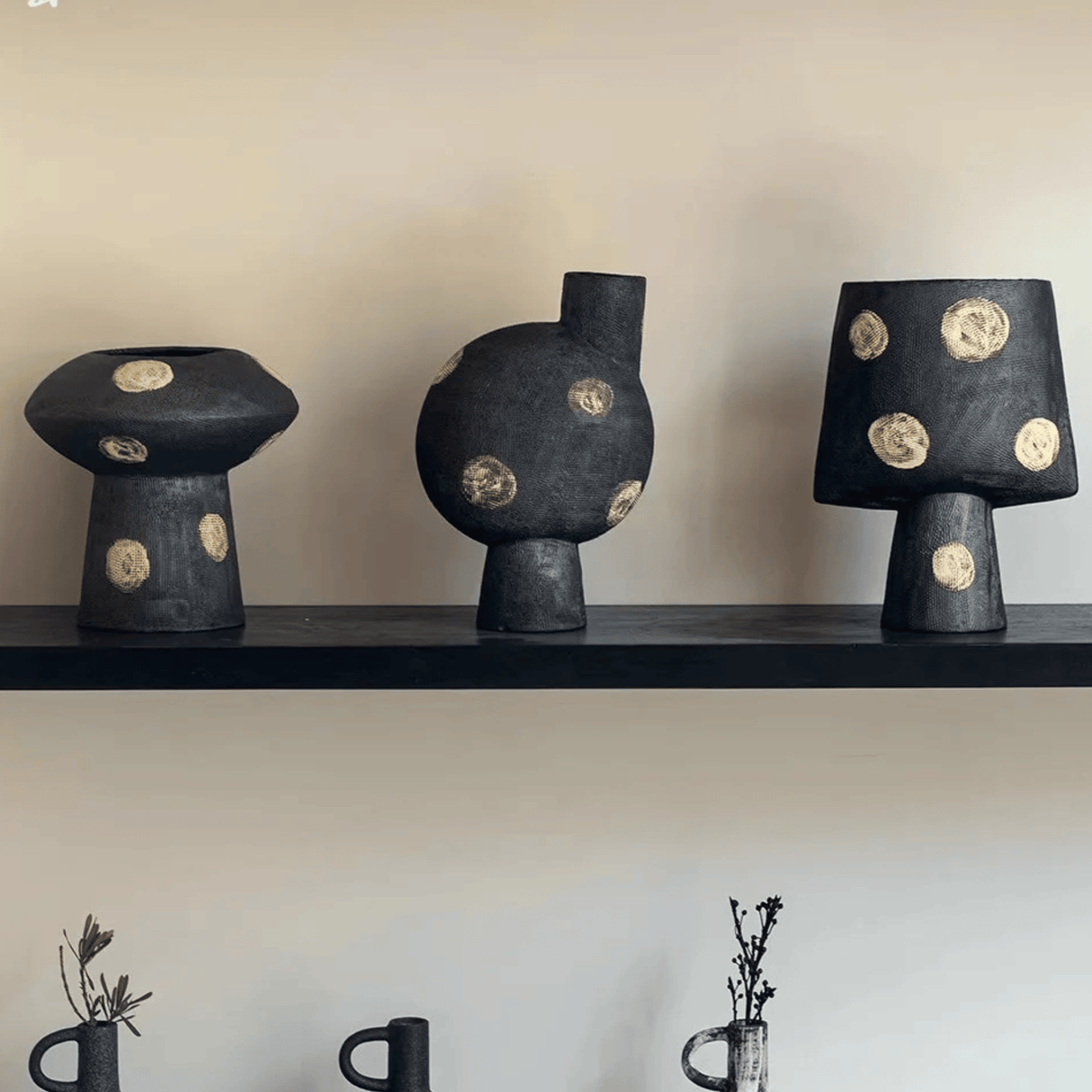Three black ceramic vases with gold circular patterns on a shelf against a plain wall.