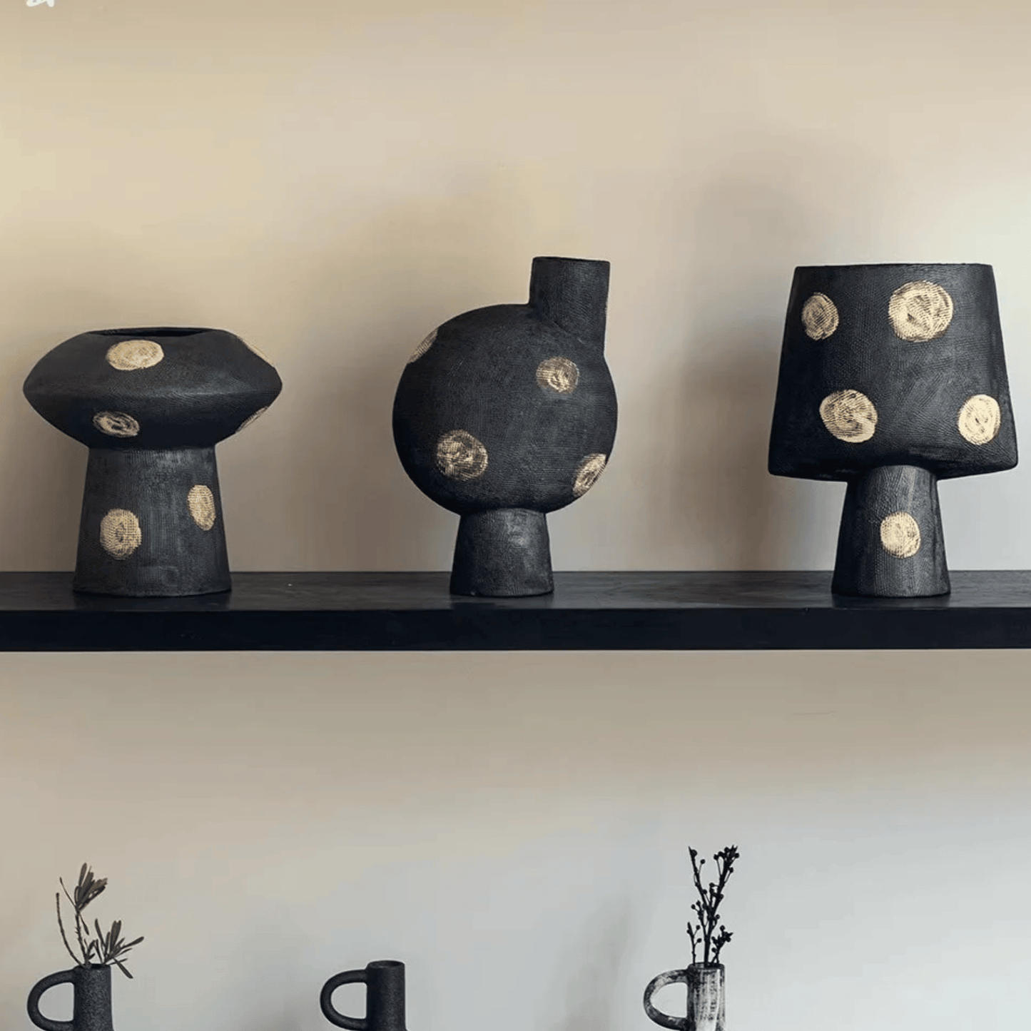 Three black ceramic vases with gold circular patterns on a shelf against a plain wall.