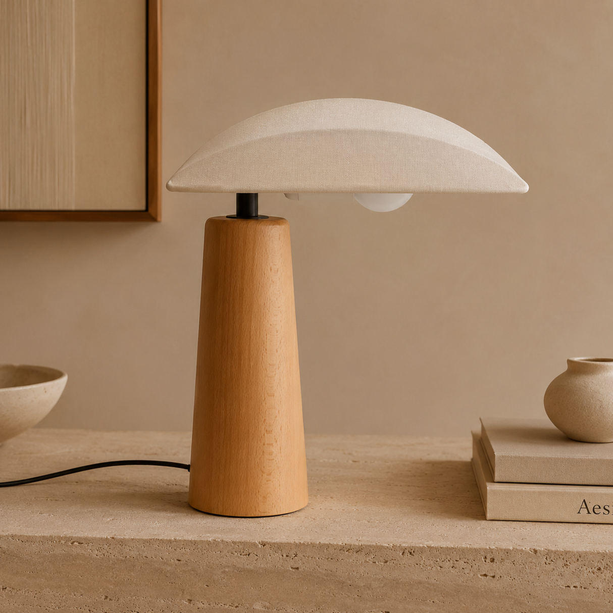 A table lamp with a tapered light wood base and a wide, dome-shaped off-white shade, styled on a stone surface with neutral decor in a warm beige room.