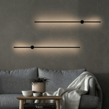 Modern wall lights on a gray wall above a gray sofa with a small table and plant.