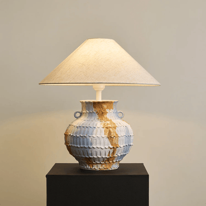 Decorative table lamp with a textured ceramic base on a dark pedestal against a neutral background