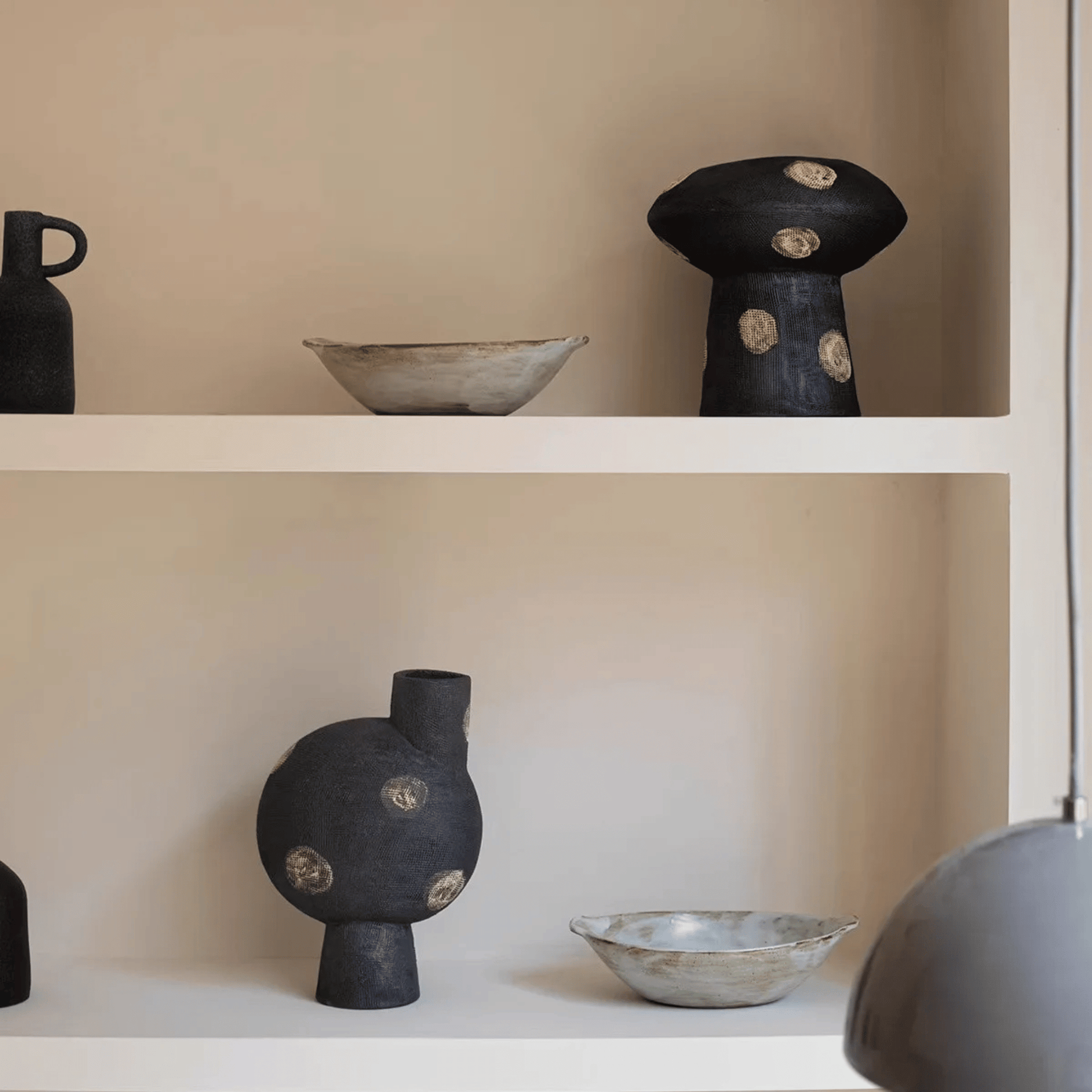 Ceramic vases and bowls on a shelf against a beige wall