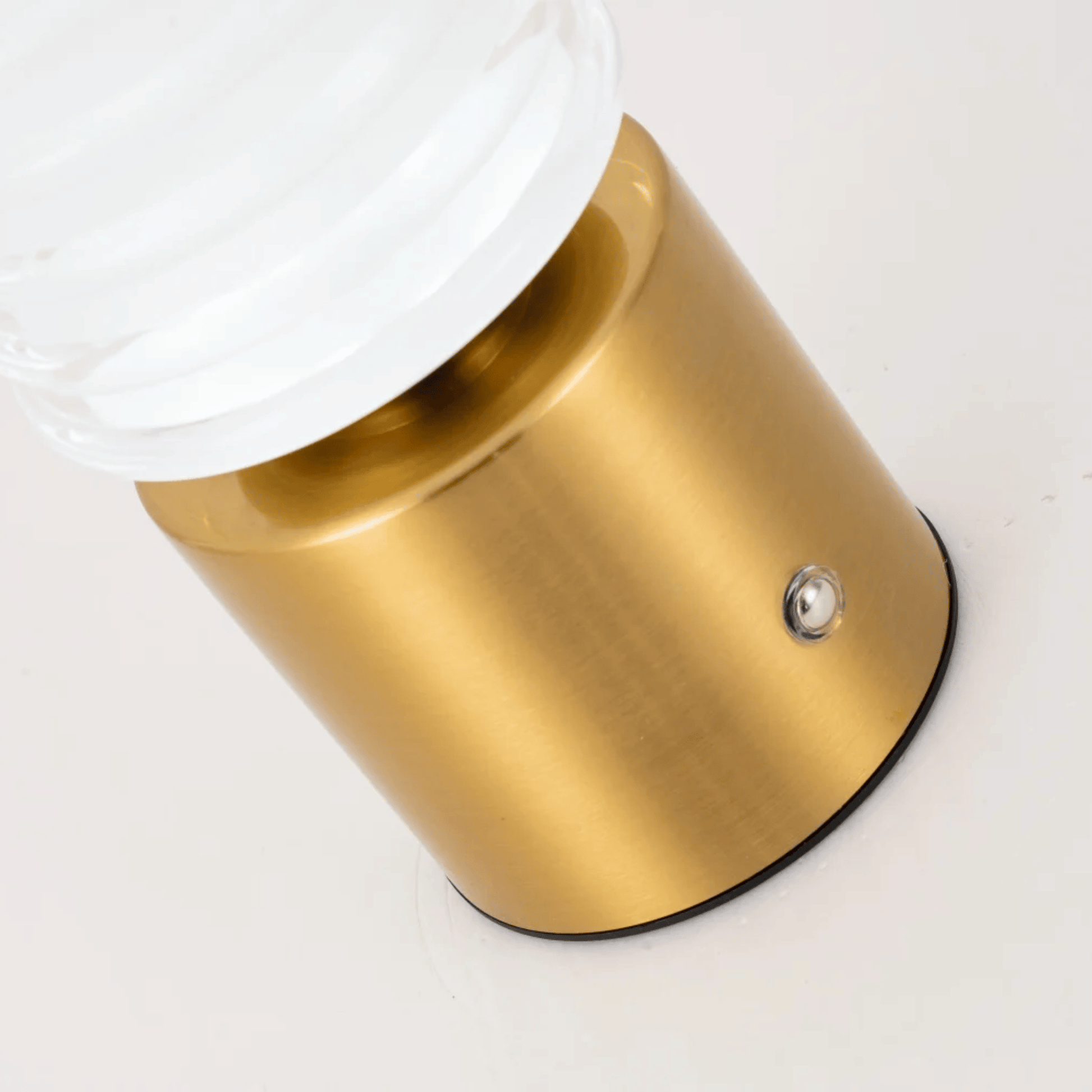 Gold cylindrical object with a white top on a light gray background
