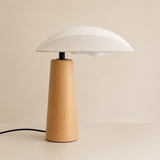 A modern mushroom-shaped table lamp with a light natural wood base and a white fabric-textured dome shade, set against a warm beige background.