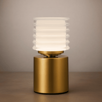 Table lamp with gold base and ribbed white glass shade on a neutral background