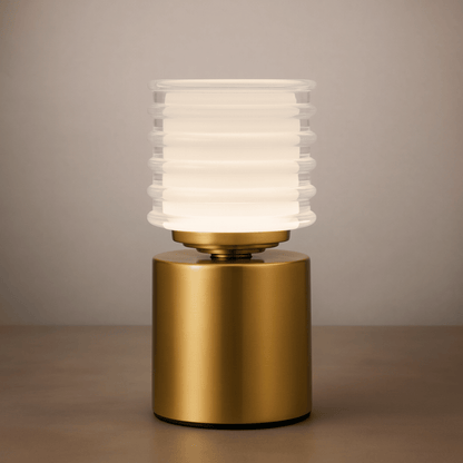 Table lamp with gold base and ribbed white glass shade on a neutral background