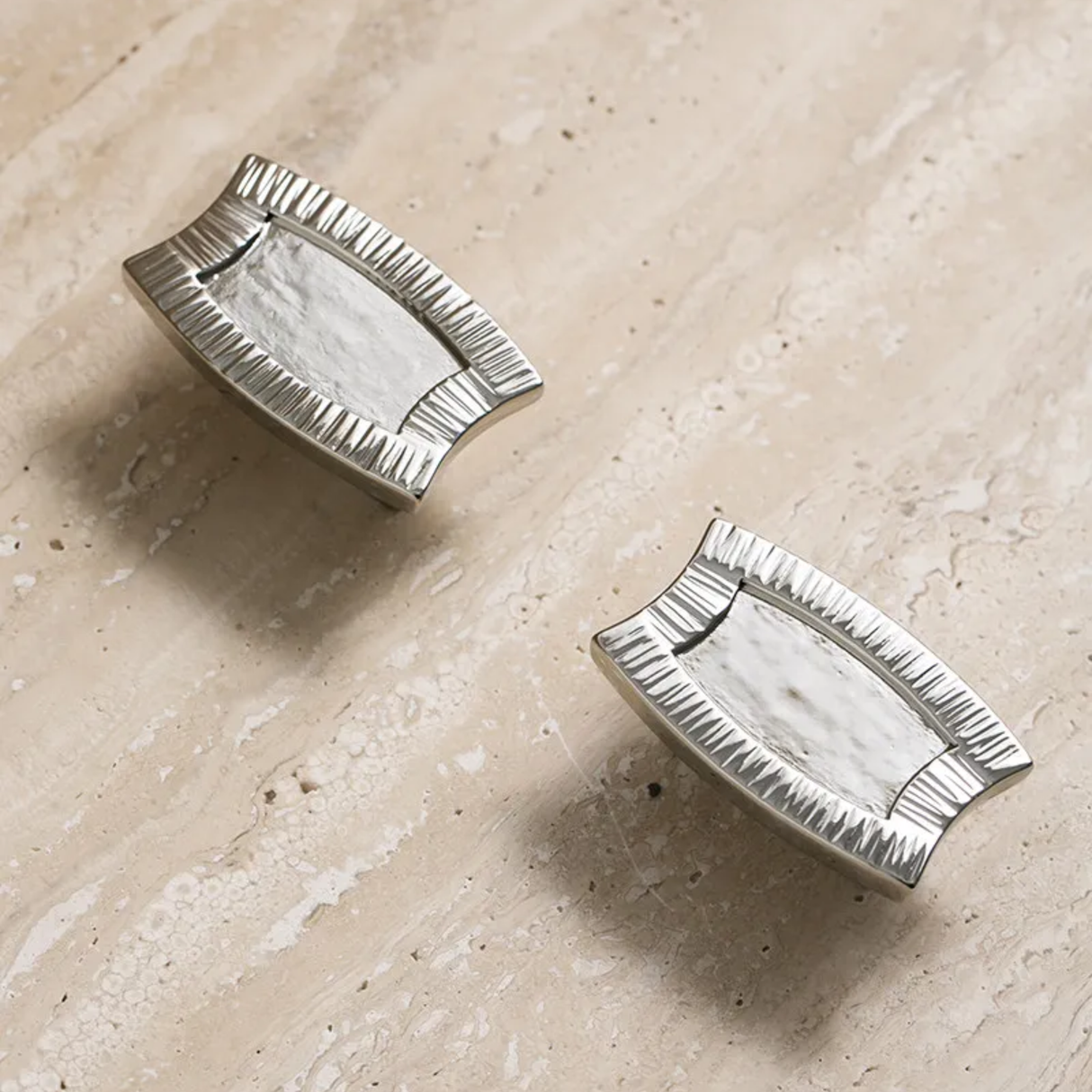 Two silver decorative items on a beige stone surface