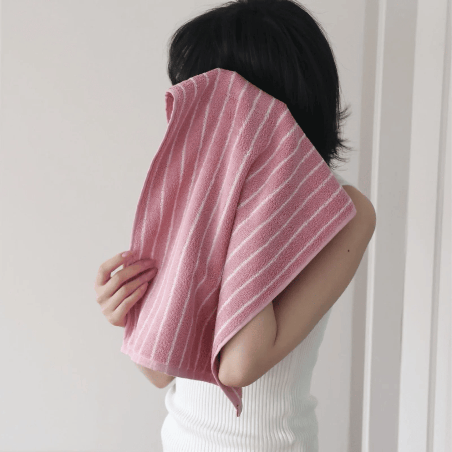 Person holding a pink striped towel in front of their face against a white background