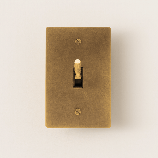 Brass-colored light switch cover with a toggle switch on a beige background