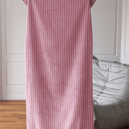 Person holding a pink and white striped towel in a room with wooden flooring and white walls.