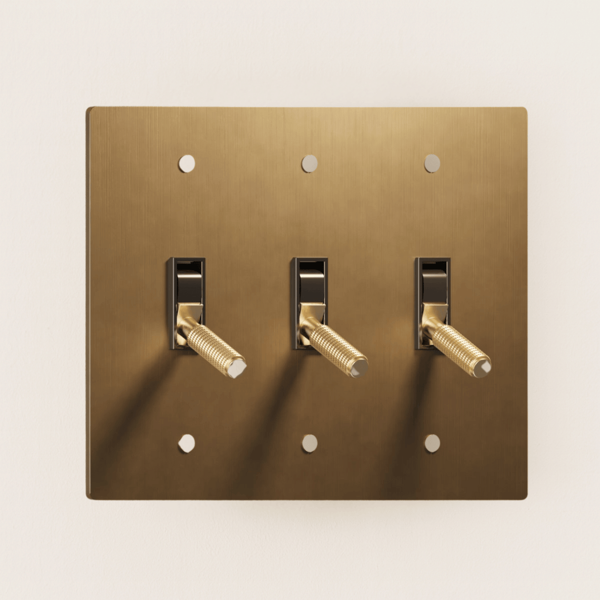 Brass light switch plate with three toggle switches on a beige background
