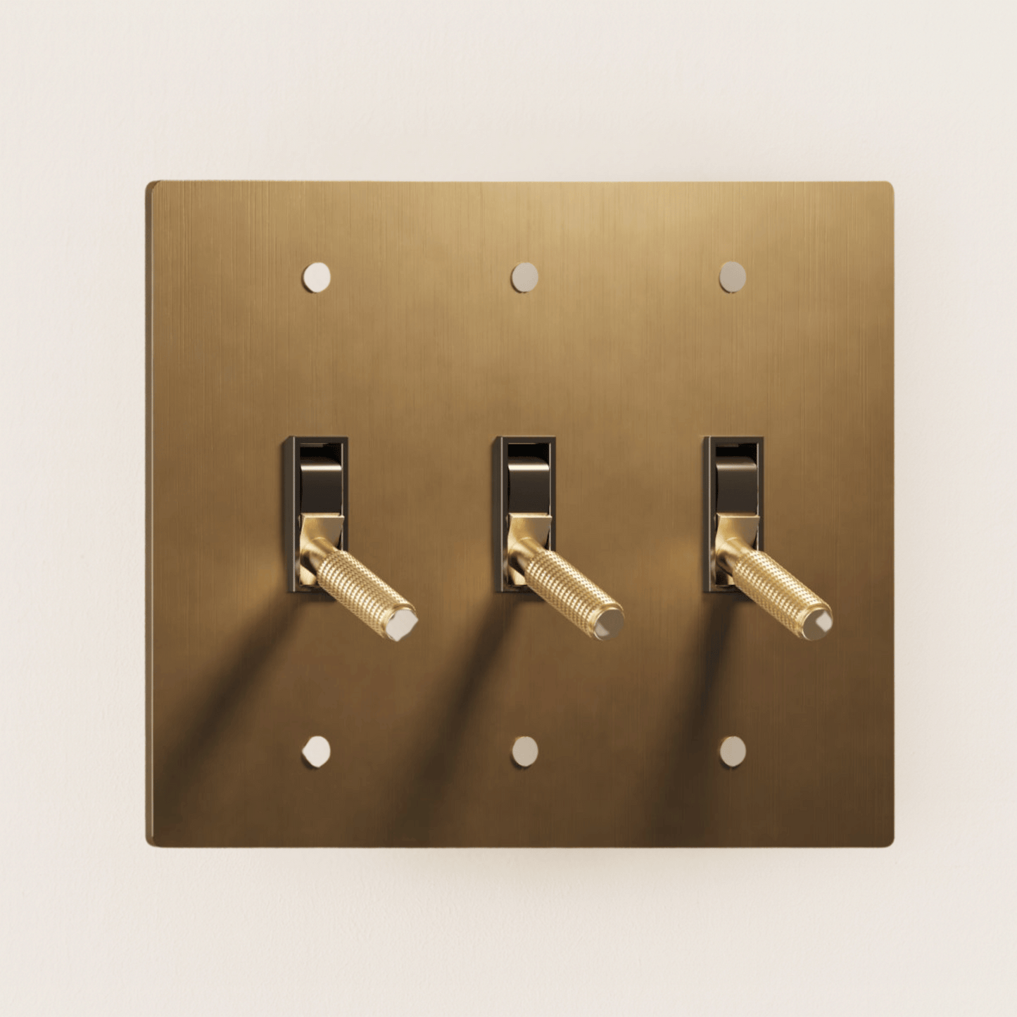 Brass light switch plate with three toggle switches on a beige background