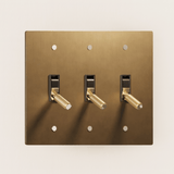 Brass light switch plate with three toggle switches on a beige background