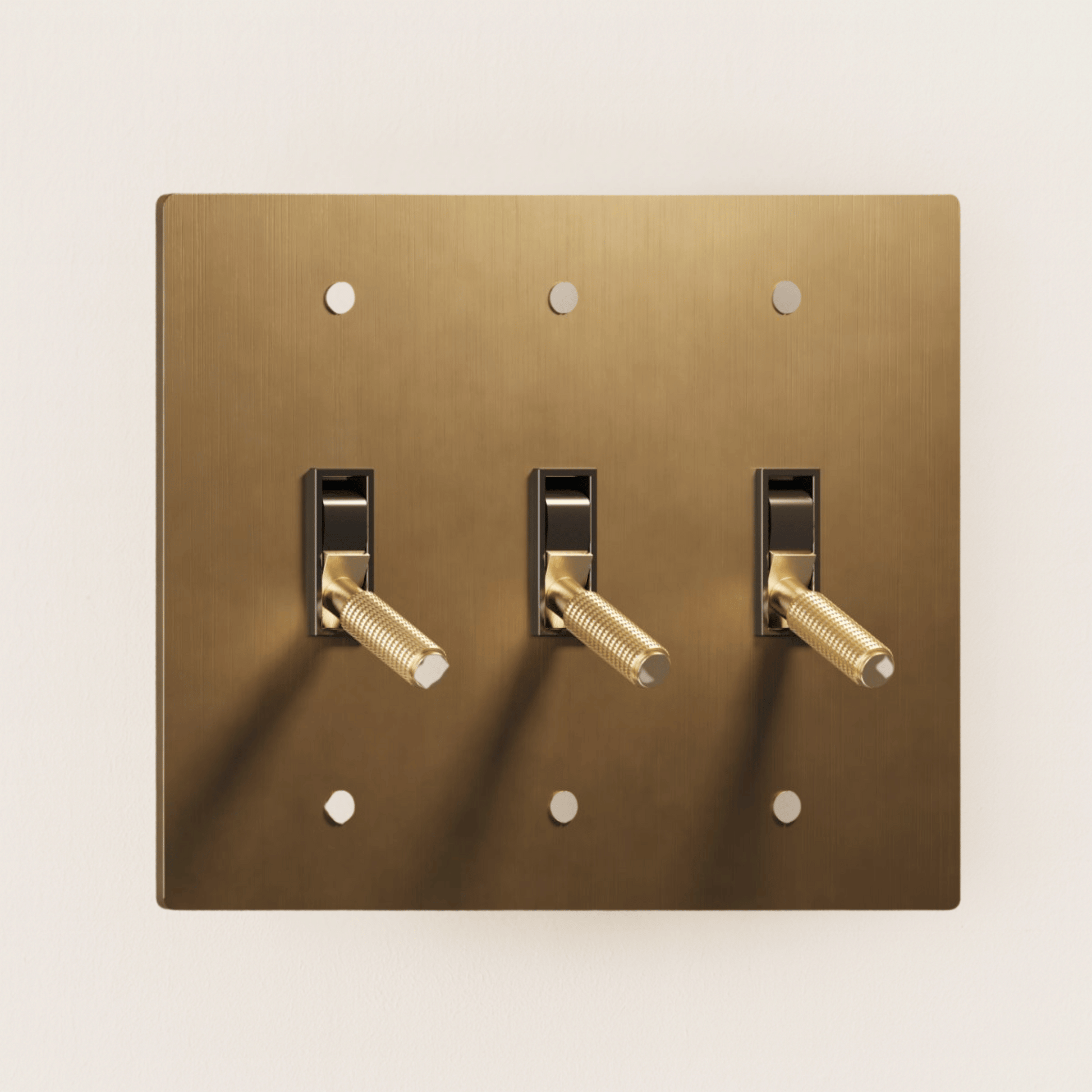 Brass light switch plate with three toggle switches on a beige background
