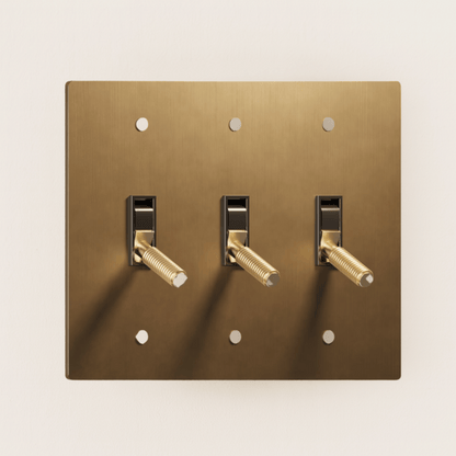 Brass light switch plate with three toggle switches on a beige background