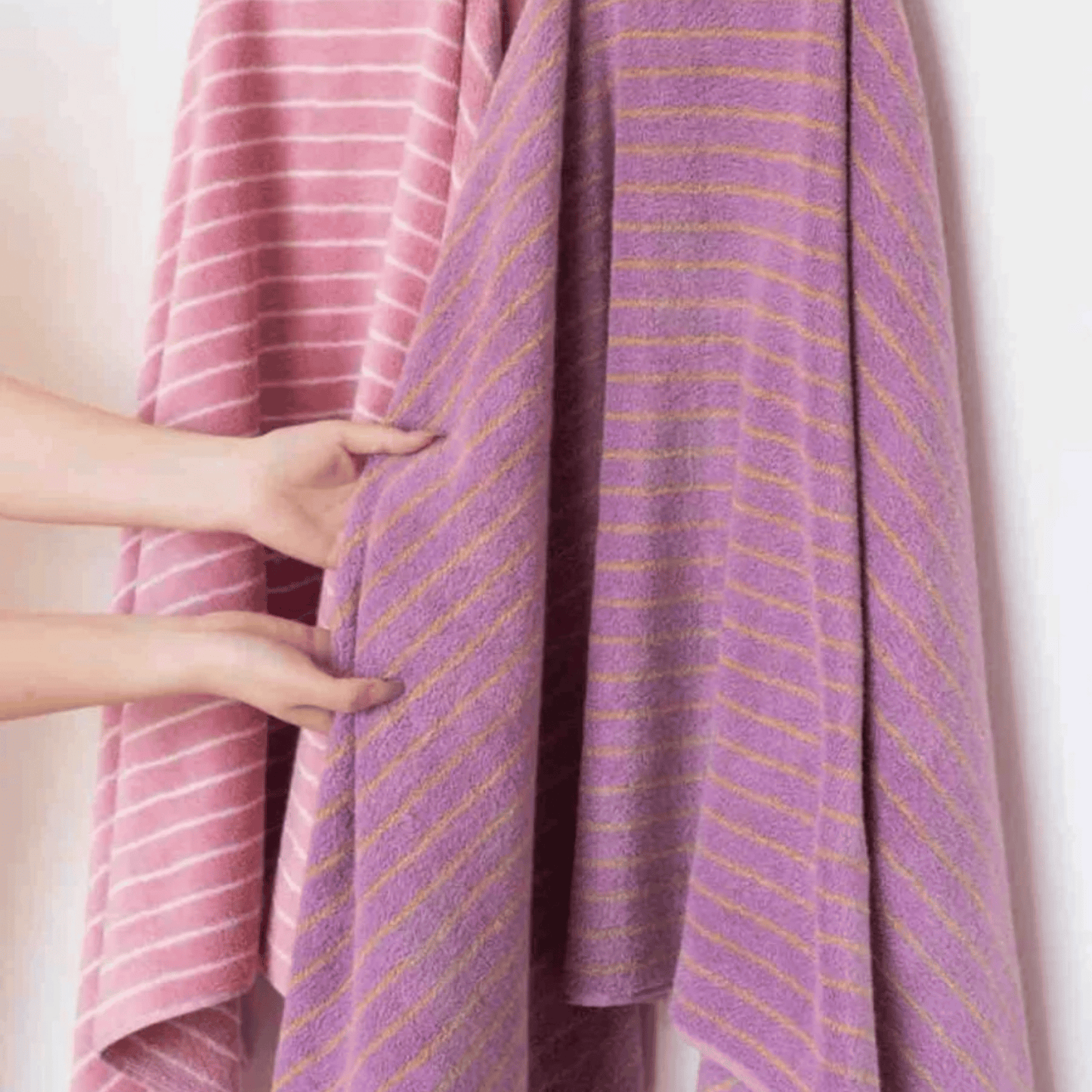 Purple towel with pink and yellow stripes draped over a person, held by hands.