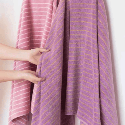 Purple towel with pink and yellow stripes draped over a person, held by hands.