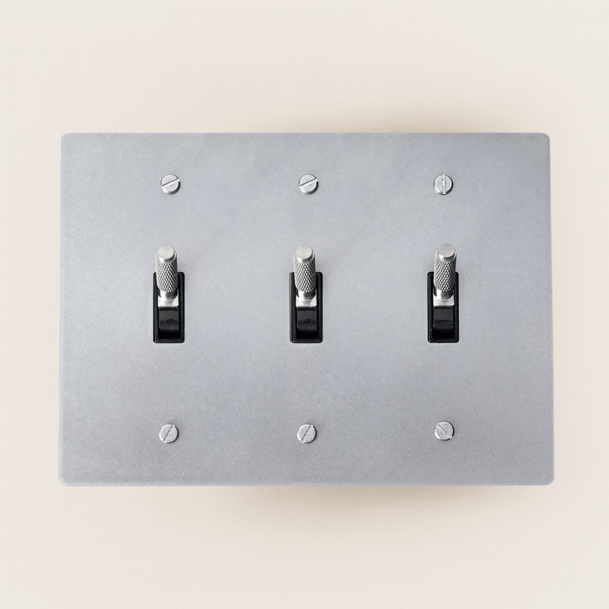 Gray light switch panel with three toggle switches on a beige wall.