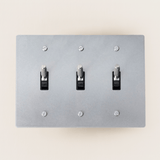 Gray light switch panel with three toggle switches on a beige wall.