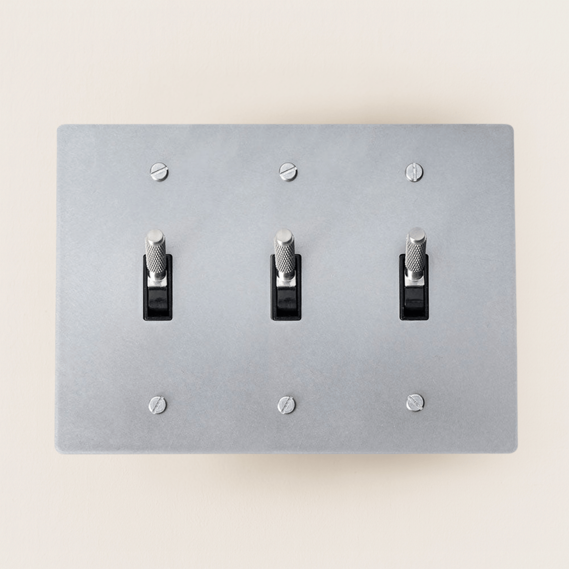 Gray light switch panel with three toggle switches on a beige wall.